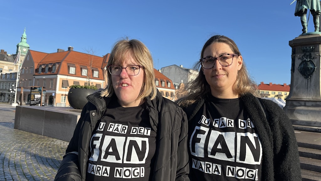 Madeleine Andersson, ansvarig för Mediaboom, står bredvid brukaren Madeleine Jerkestrand på ett torg med historiska byggnader och staty i bakgrunden, båda klädda i svarta tröjor med text.
