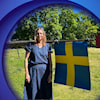 A woman in a summer dress stood by a pole with a Sweden flag.