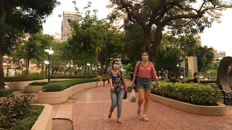 Två personer med munskydd går i en park i Bangkok.
